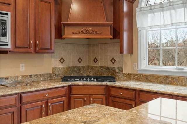 kitchen with light stone counters, decorative backsplash, premium range hood, and appliances with stainless steel finishes