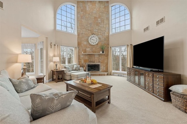 living room featuring a towering ceiling, a stone fireplace, and light carpet