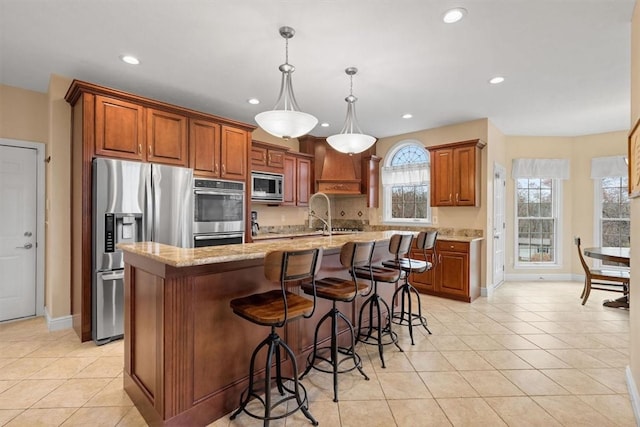 kitchen featuring stainless steel appliances, light stone countertops, light tile patterned floors, a kitchen island with sink, and pendant lighting