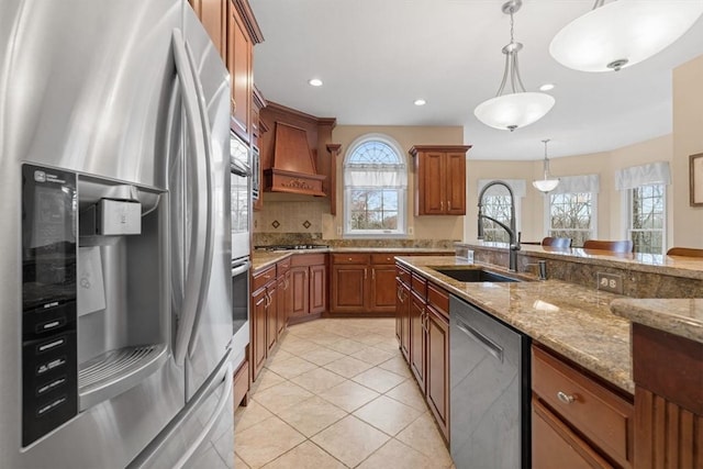 kitchen featuring stainless steel appliances, sink, light stone counters, custom range hood, and hanging light fixtures