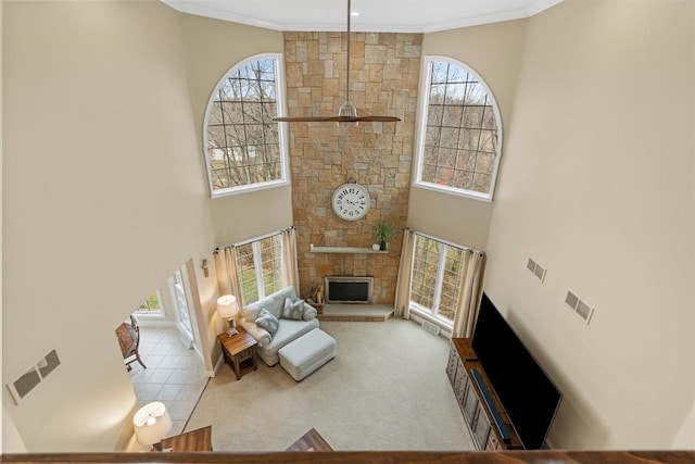 living room featuring a stone fireplace, a high ceiling, and crown molding