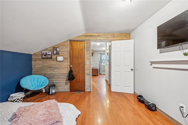 bedroom featuring lofted ceiling, hardwood / wood-style flooring, and wooden walls