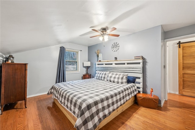 bedroom featuring ceiling fan, a barn door, vaulted ceiling, and light hardwood / wood-style flooring