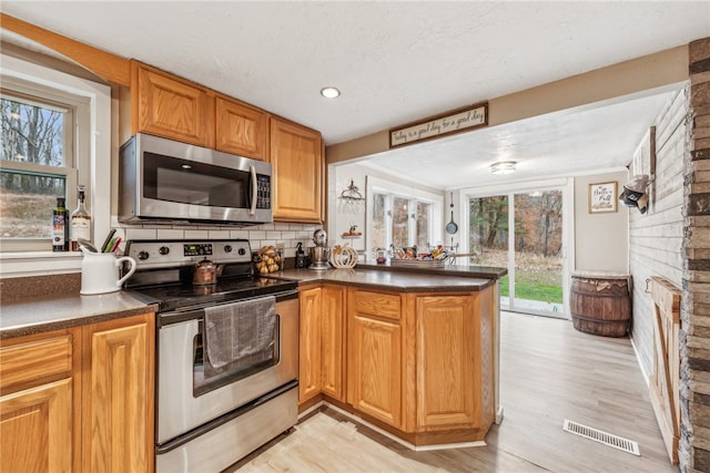 kitchen with kitchen peninsula, tasteful backsplash, stainless steel appliances, a fireplace, and light hardwood / wood-style floors