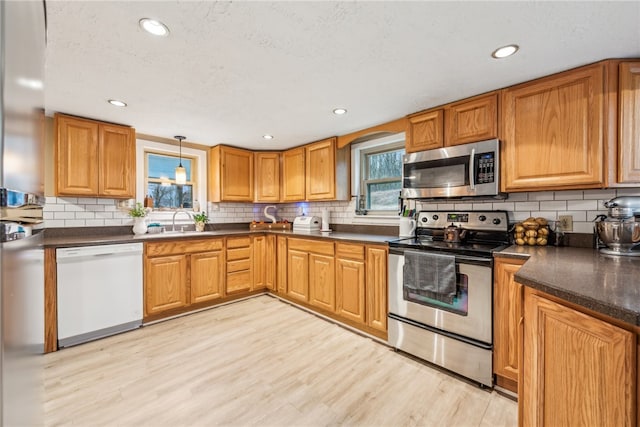 kitchen featuring backsplash, sink, light hardwood / wood-style flooring, decorative light fixtures, and stainless steel appliances