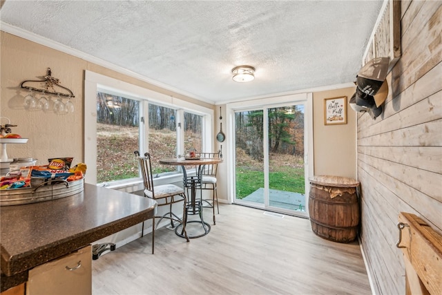 dining space with light hardwood / wood-style floors, ornamental molding, and a textured ceiling