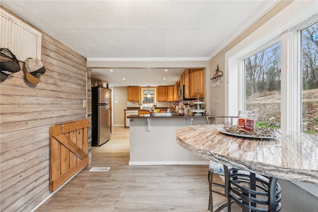 kitchen with a kitchen breakfast bar, light hardwood / wood-style flooring, kitchen peninsula, decorative backsplash, and appliances with stainless steel finishes