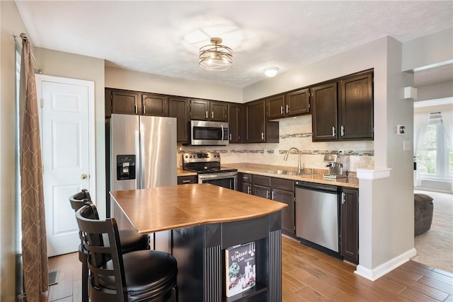 kitchen featuring dark brown cabinetry, light wood-type flooring, stainless steel appliances, and a kitchen island