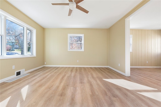 unfurnished room with ornamental molding, light hardwood / wood-style floors, wood walls, and ceiling fan