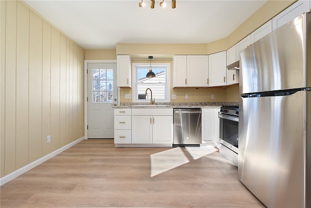 kitchen featuring stainless steel appliances, sink, light wood-type flooring, white cabinets, and pendant lighting