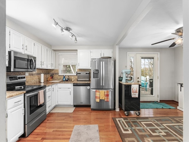 kitchen with stainless steel appliances, backsplash, light stone countertops, light hardwood / wood-style floors, and white cabinets