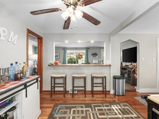 kitchen with a kitchen breakfast bar, light hardwood / wood-style floors, ceiling fan, and white cabinets