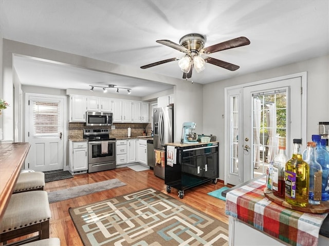 kitchen with white cabinetry, decorative backsplash, appliances with stainless steel finishes, and light hardwood / wood-style floors