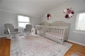 bedroom featuring lofted ceiling, hardwood / wood-style floors, and a crib