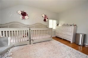 bedroom with a crib, lofted ceiling, and hardwood / wood-style flooring