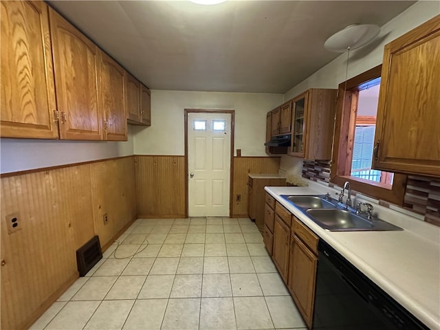 kitchen featuring light tile patterned floors, sink, black dishwasher, and wood walls