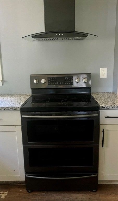 room details with stainless steel electric range, dark hardwood / wood-style flooring, white cabinets, wall chimney exhaust hood, and light stone countertops