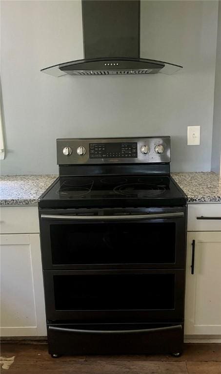 3036 Mcneal Rd, Hampton, PA 15101 - detailed view of double oven range, wall chimney range hood, dark wood-type flooring, white cabinetry, and light stone countertops