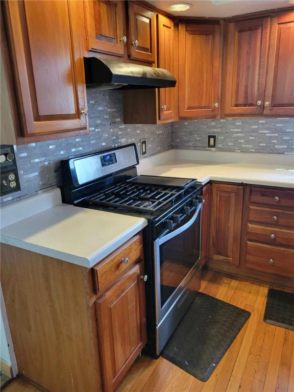 kitchen with stainless steel range with gas stovetop, light hardwood / wood-style floors, and tasteful backsplash