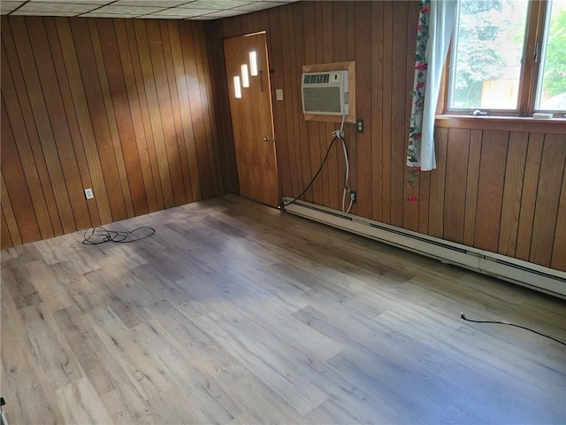 empty room with a baseboard radiator, light hardwood / wood-style floors, and wooden walls