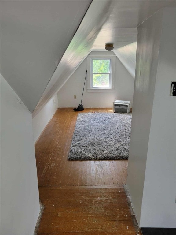 additional living space featuring hardwood / wood-style floors, an AC wall unit, and vaulted ceiling