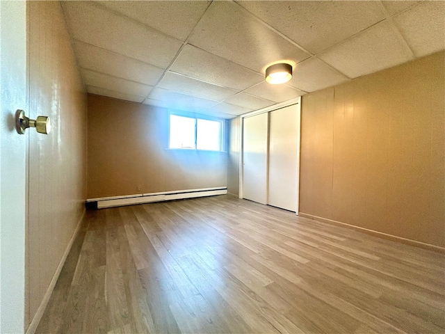 basement with a paneled ceiling, wood-type flooring, and a baseboard radiator