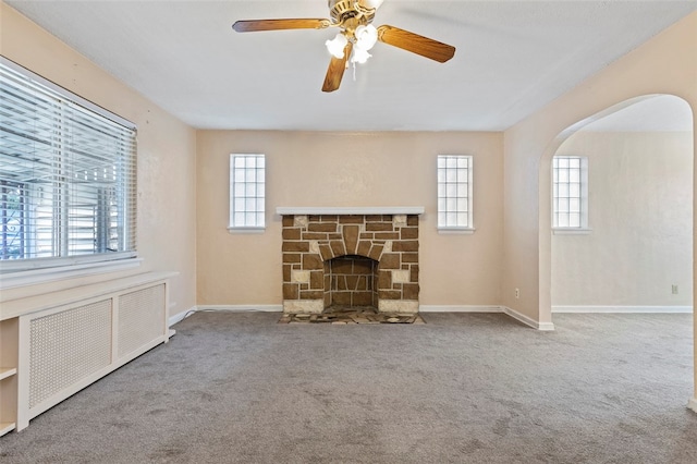 unfurnished living room with a stone fireplace, plenty of natural light, radiator heating unit, and carpet