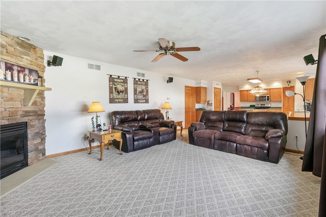 living room featuring ceiling fan, a stone fireplace, and light colored carpet