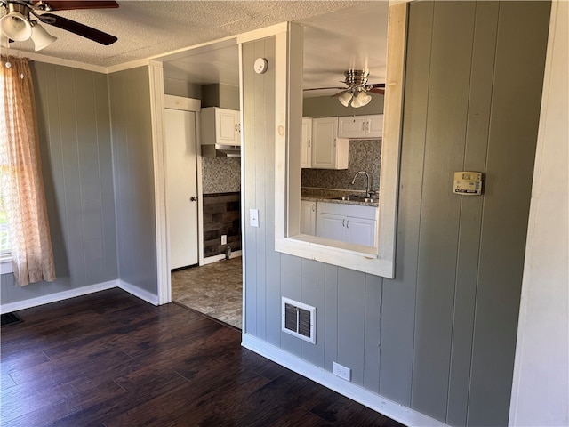 kitchen featuring dark wood-type flooring, wood walls, sink, stone countertops, and white cabinetry