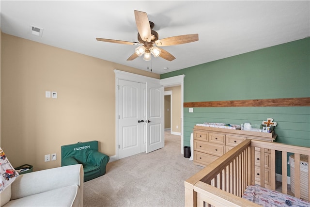 carpeted bedroom with ceiling fan, a closet, a nursery area, and wood walls