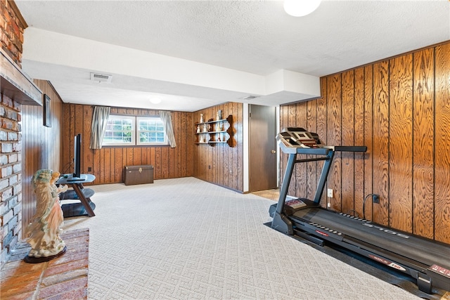 exercise room with a textured ceiling, wooden walls, and light carpet