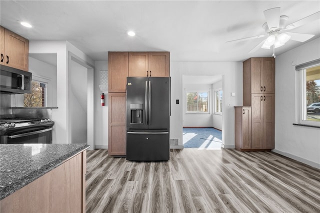 kitchen with stainless steel appliances, light hardwood / wood-style flooring, ceiling fan, and dark stone counters