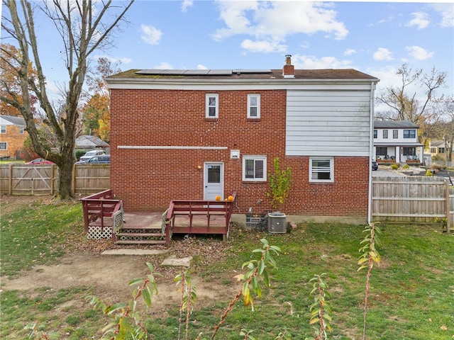 rear view of house with solar panels, a yard, a deck, and central AC