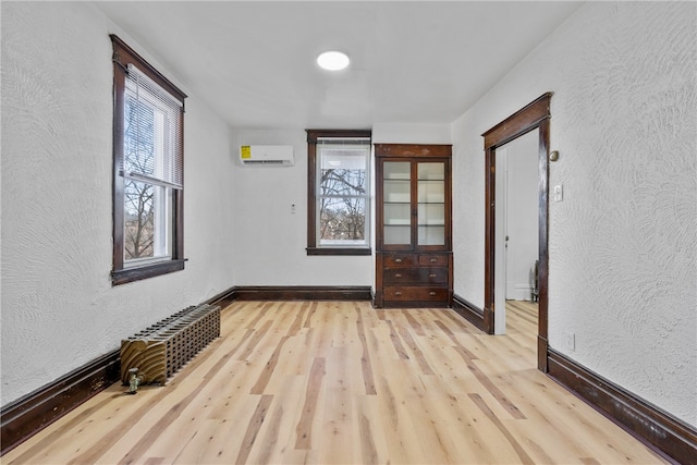 empty room featuring a wall mounted AC and light hardwood / wood-style flooring