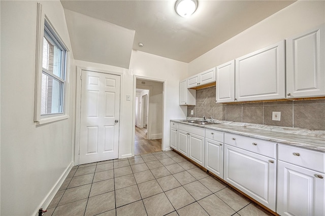 kitchen featuring tasteful backsplash, white cabinetry, light stone countertops, and light tile patterned flooring