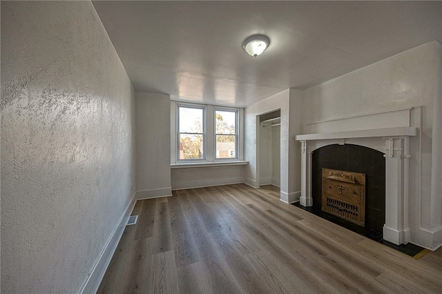 unfurnished living room with a tiled fireplace and wood-type flooring