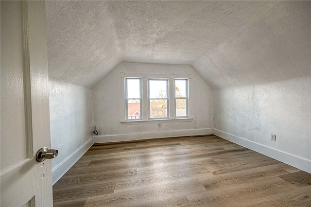 additional living space featuring hardwood / wood-style floors, vaulted ceiling, and a textured ceiling