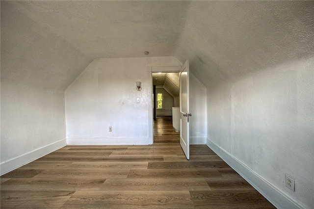 additional living space with a textured ceiling, hardwood / wood-style flooring, and vaulted ceiling