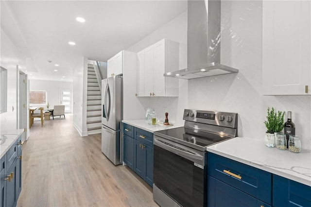 kitchen with white cabinets, wall chimney exhaust hood, blue cabinetry, light hardwood / wood-style floors, and stainless steel appliances