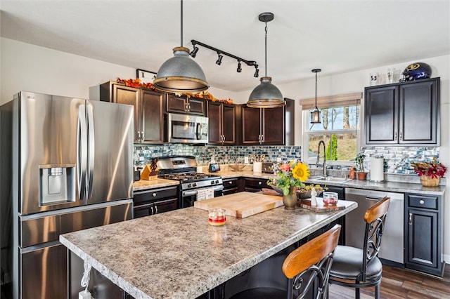 kitchen featuring appliances with stainless steel finishes, dark hardwood / wood-style floors, hanging light fixtures, sink, and a center island