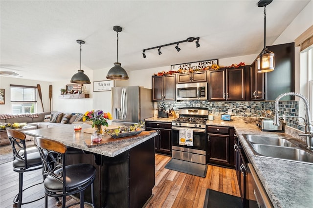 kitchen featuring stainless steel appliances, sink, a kitchen breakfast bar, hanging light fixtures, and light wood-type flooring