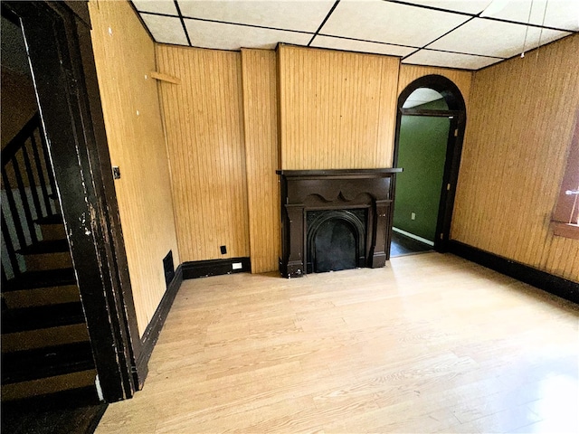 unfurnished living room with a paneled ceiling, wood walls, and light hardwood / wood-style flooring