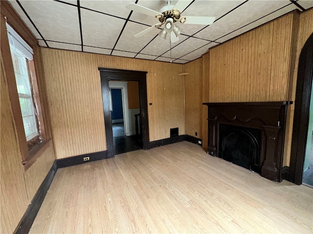 unfurnished living room with wood walls, ceiling fan, and light wood-type flooring