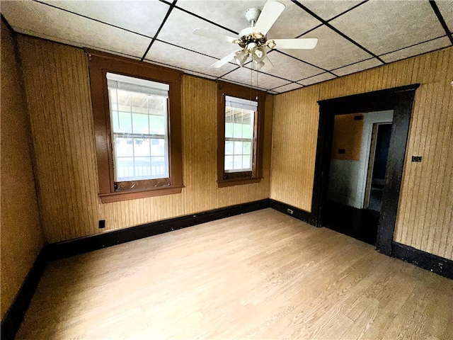 empty room featuring a paneled ceiling, ceiling fan, wooden walls, and light hardwood / wood-style flooring