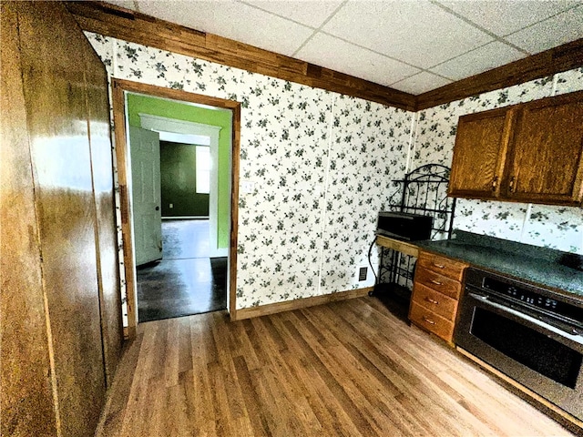 kitchen with hardwood / wood-style floors, wall oven, and a drop ceiling