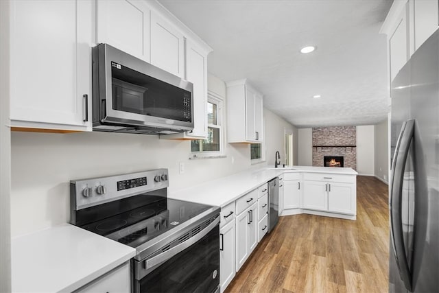 kitchen featuring white cabinetry, a fireplace, stainless steel appliances, and light hardwood / wood-style flooring