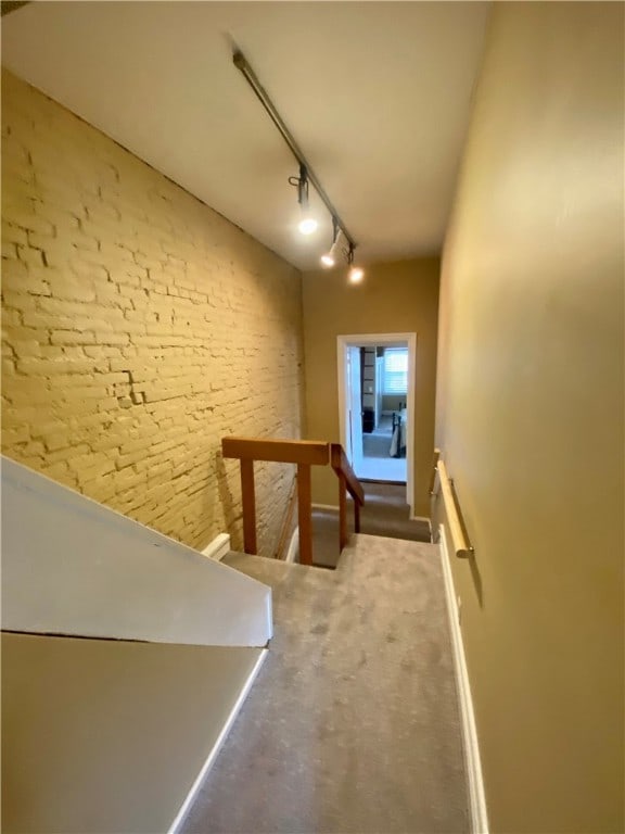 corridor featuring rail lighting, brick wall, and an upstairs landing