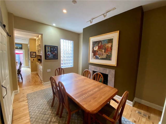 dining room featuring light wood finished floors, a barn door, baseboards, a tile fireplace, and rail lighting