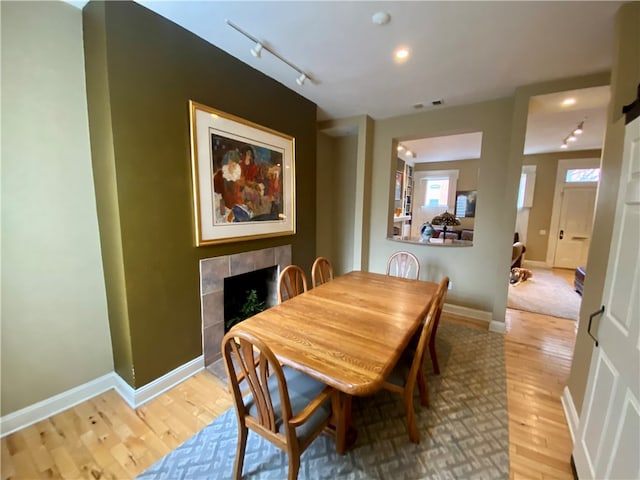 dining space featuring visible vents, baseboards, a tiled fireplace, light wood-style floors, and track lighting