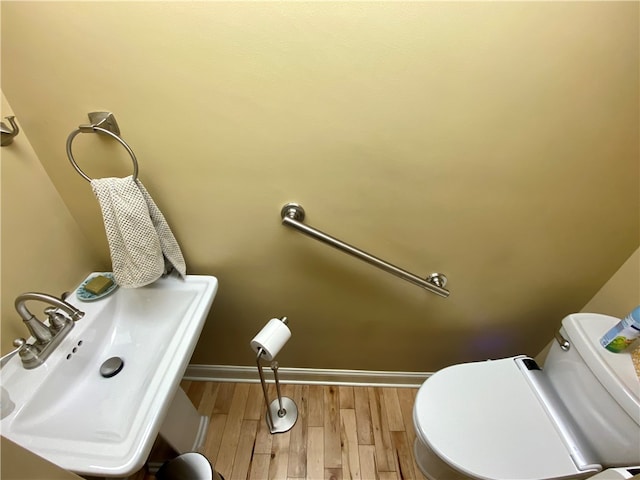 half bath featuring baseboards, a sink, toilet, and wood finished floors